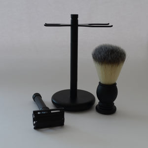 A black stand with a black razor and a black handled shaving brush next to it