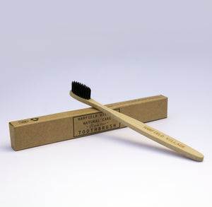 A natural coloured bamboo toothbrush with black bristles resting on a kraft cardboard box 